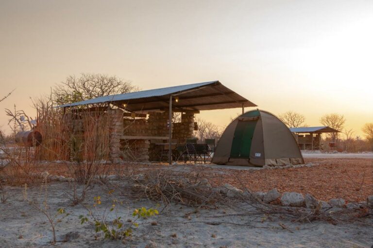 Tents pitched beside a stone braai shelter at sunset at Etosha Trading Post Campsite